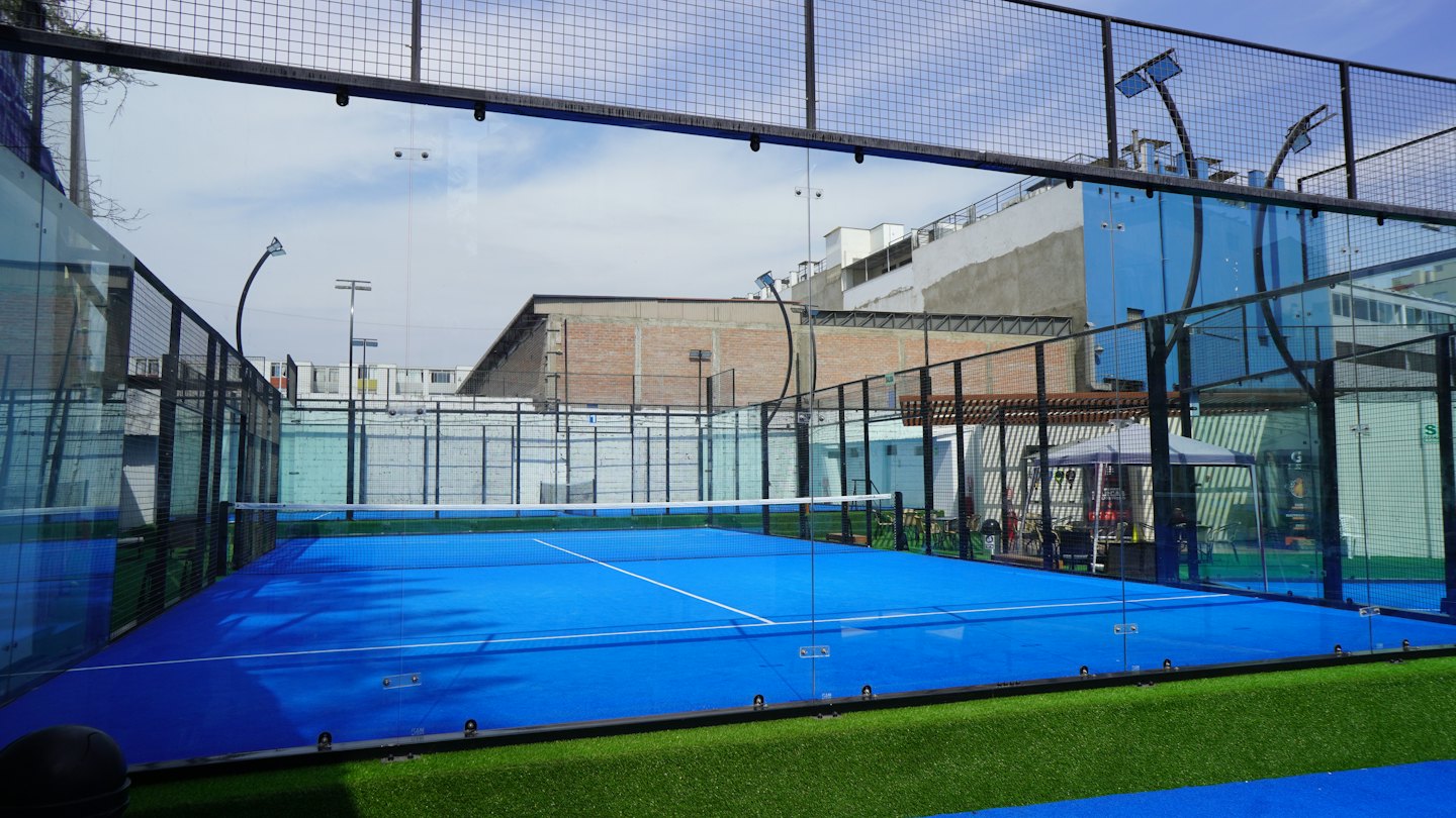 Campo da padel vuoto con superficie blu e pareti di vetro.