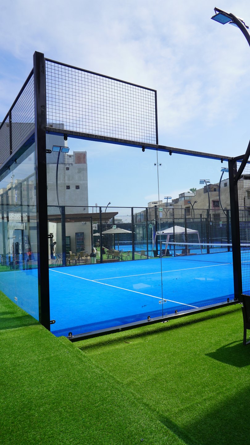 Campo da padel vuoto con superficie blu e pareti di vetro.
