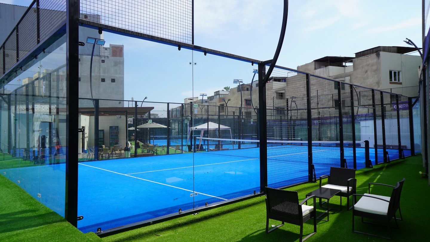 Campo da padel vuoto con superficie blu e pareti di vetro.