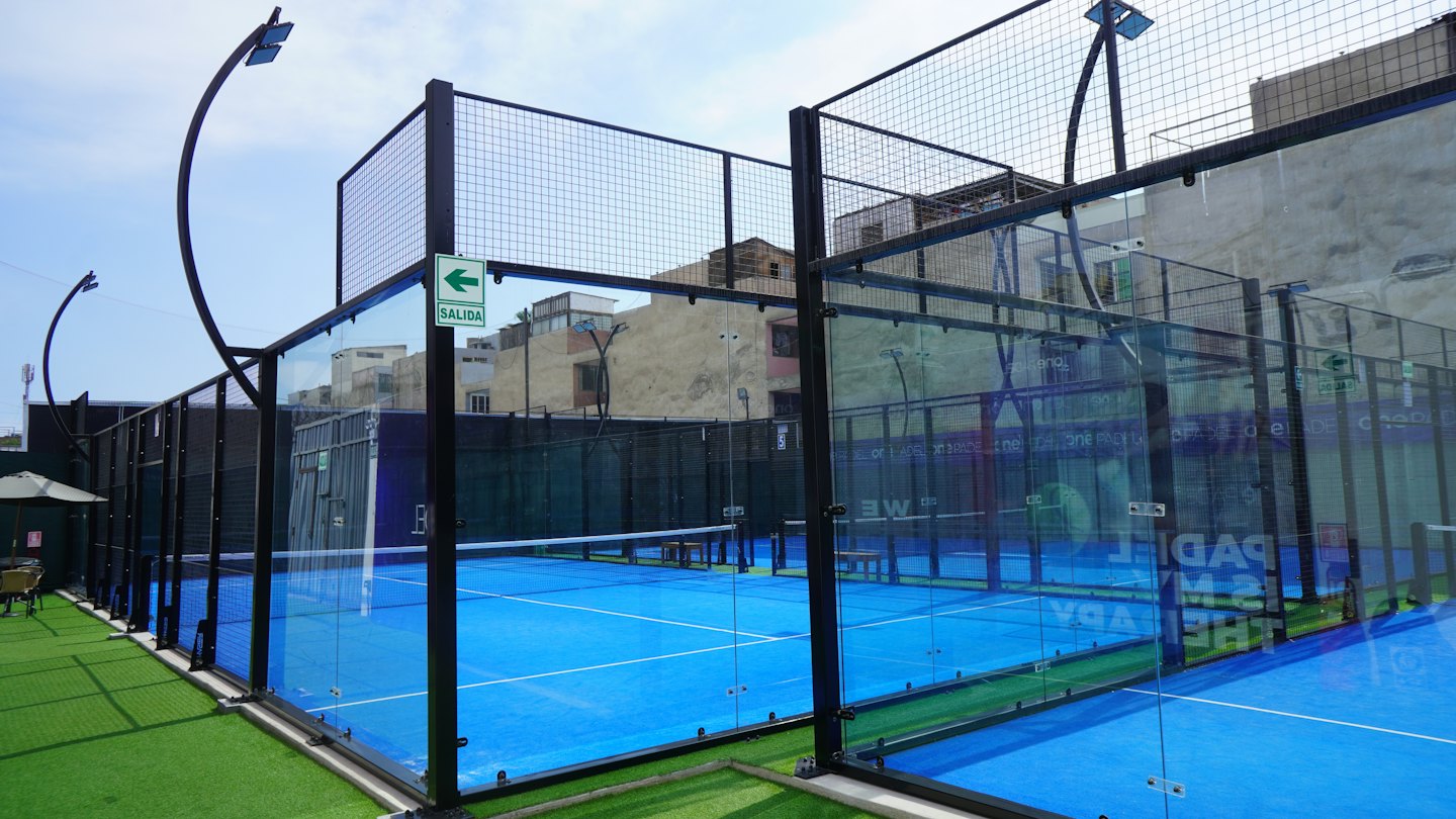 Campo da padel vuoto all'aperto con pavimento blu e pareti di vetro.