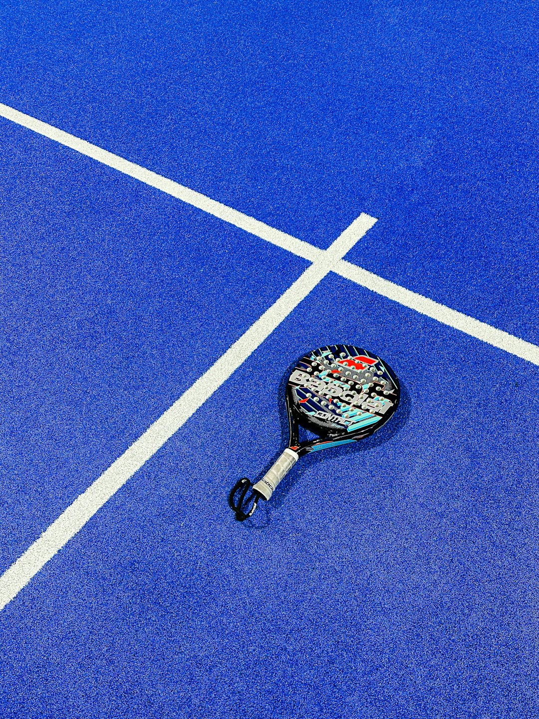 Racchetta da padel appoggiata su un campo blu brillante.